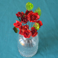 Un joli bouquet de neuf roses rouges et six feuilles vertes en verre de Murano sur fond bleu 